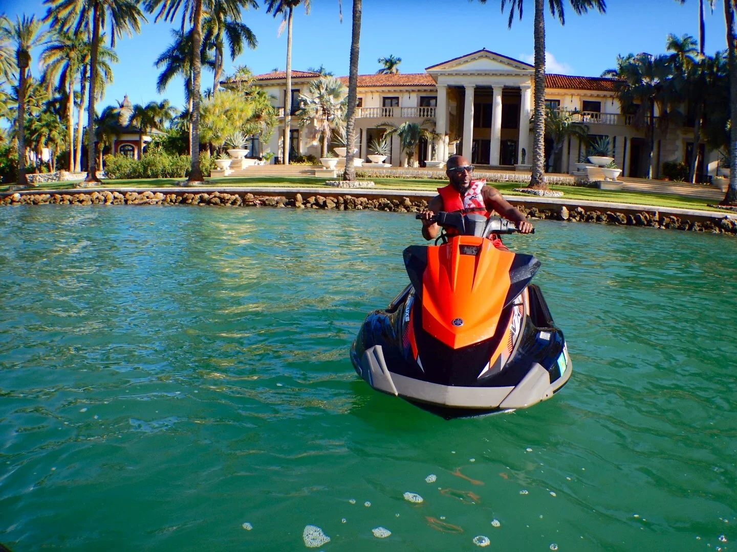 Rider on an orange jet ski in front of a waterfront mansion in Miami